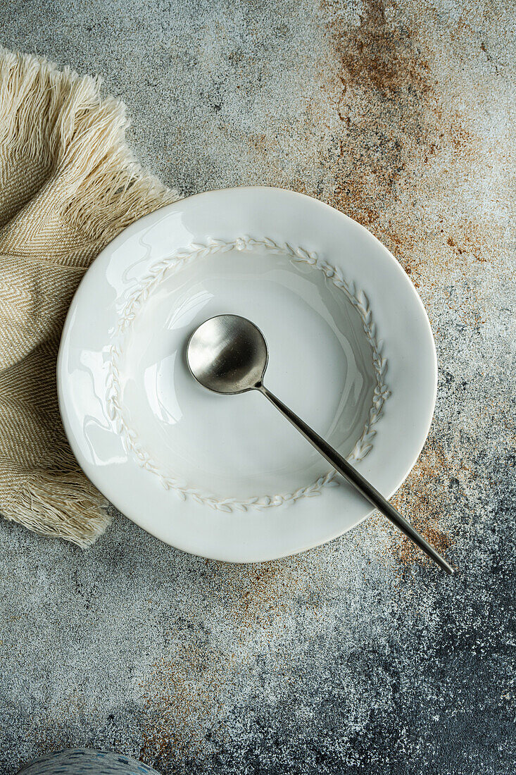 Top view of autumnal table setting with white ceramic bowl and spoon on napkin against gray surface