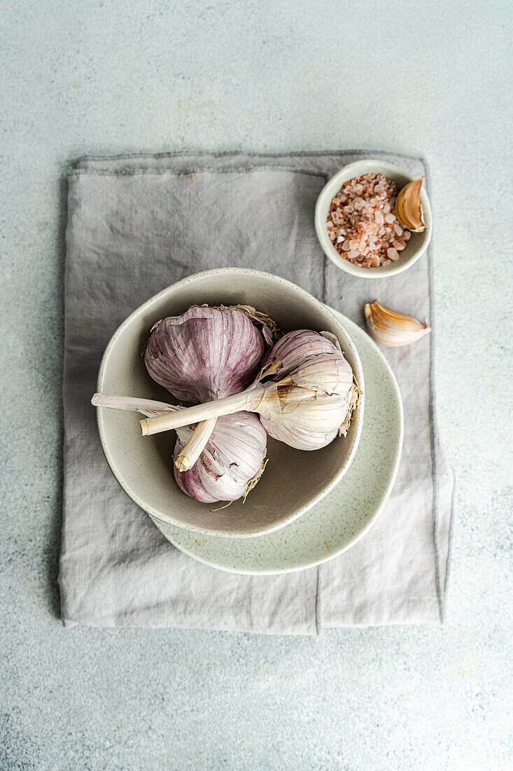 Top view of raw garlic heads in the bowl as a cooking ingredient on concrete background