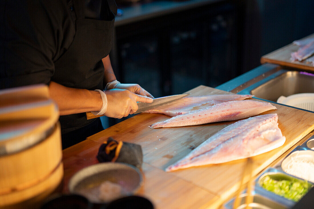 A sushi chef meticulously slices fish at a dimly lit sushi bar, showcasing the art of Japanese cuisine.