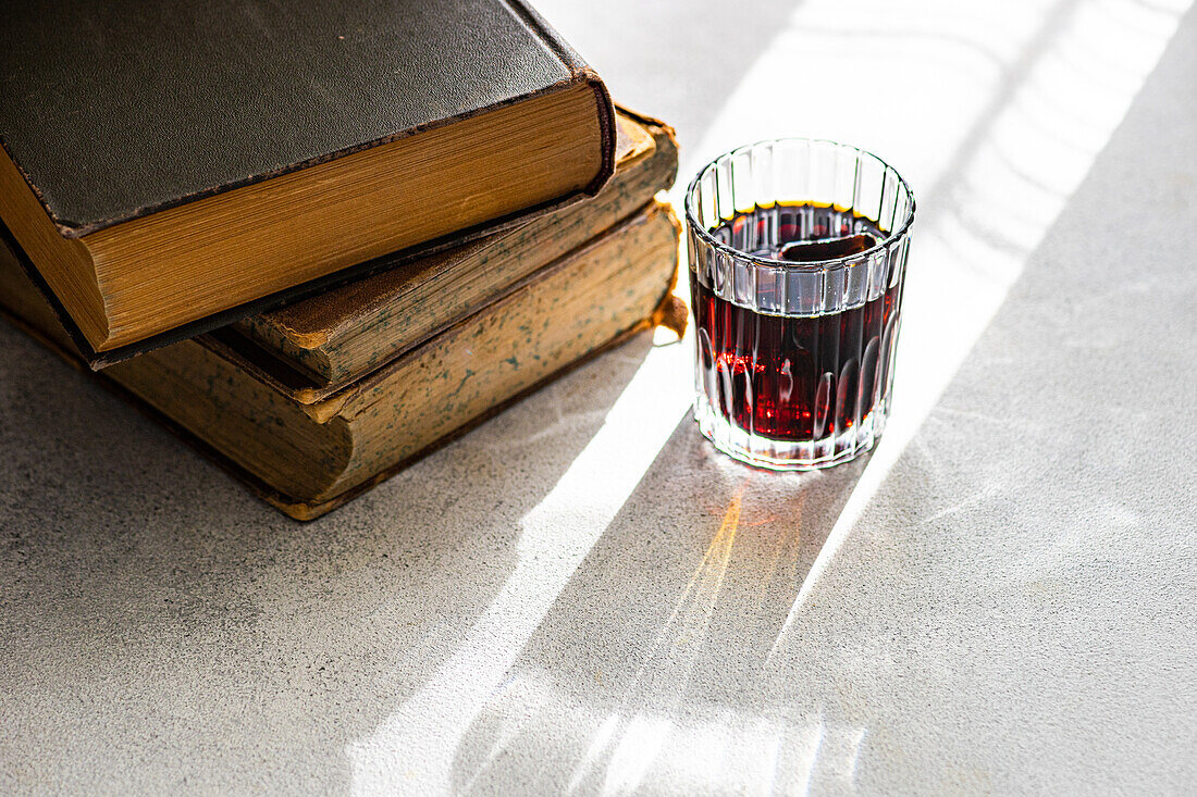 Cherry liqueur in a clear glass beside a stack of vintage books on a sunlit surface