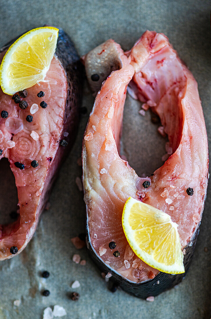 Top view of fresh trout steaks arranged on baking paper, ready to be cooked with Slices of lemon, salt and pepper