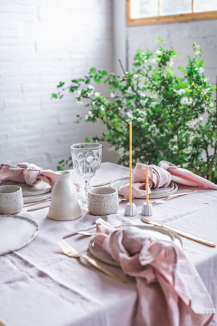 Gedeckter Tisch mit Tischtuch und Geschirr in der Nähe von Gläsern für ein Bankett in einem hellen, mit grünen Topfpflanzen dekorierten Raum