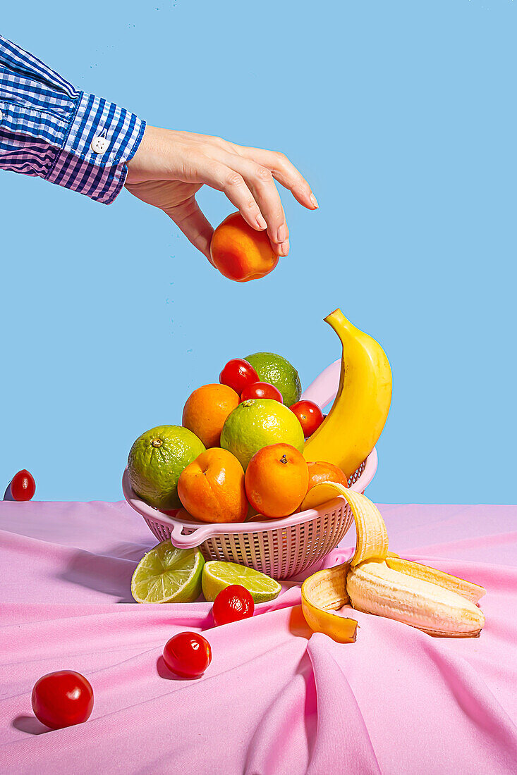 Anonymous person taking a peach of plastic drying rack with fresh fruit on a table with a pink tablecloth