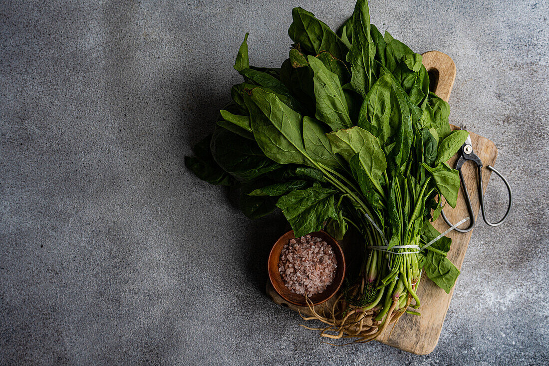 Draufsicht auf ein Bündel frischer Spinatblätter auf einem rustikalen Holzbrett, begleitet von aromatischen Gewürzen in einer Schüssel, die die Zubereitung eines gesunden Salats symbolisiert