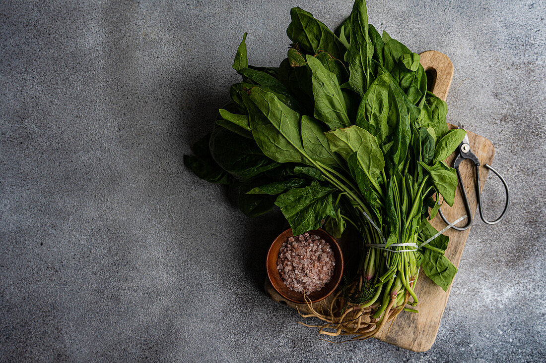 Top view of bunch of fresh spinach leaves on rustic wooden board accompanied by aromatic spices in bowl symbolizing healthy salad preparation