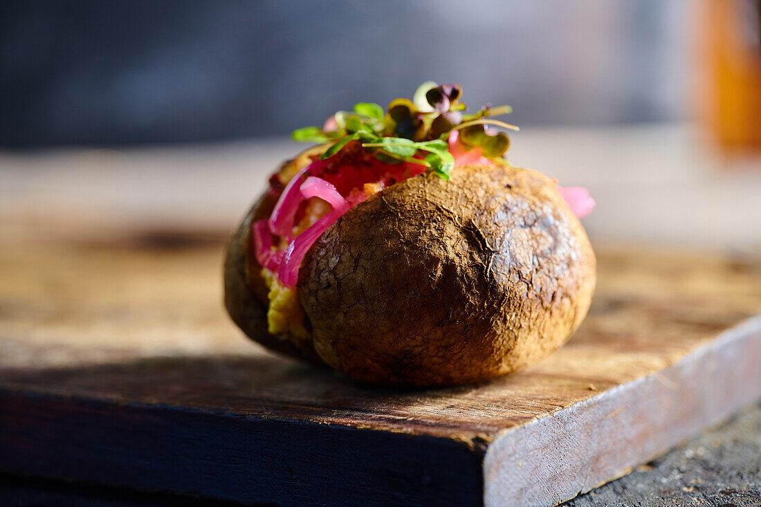 Appetitliche traditionelle ecuadorianische Kumpir-Kartoffel mit Füllung und Kräutern auf einem hölzernen Schneidebrett vor einem unscharfen Hintergrund