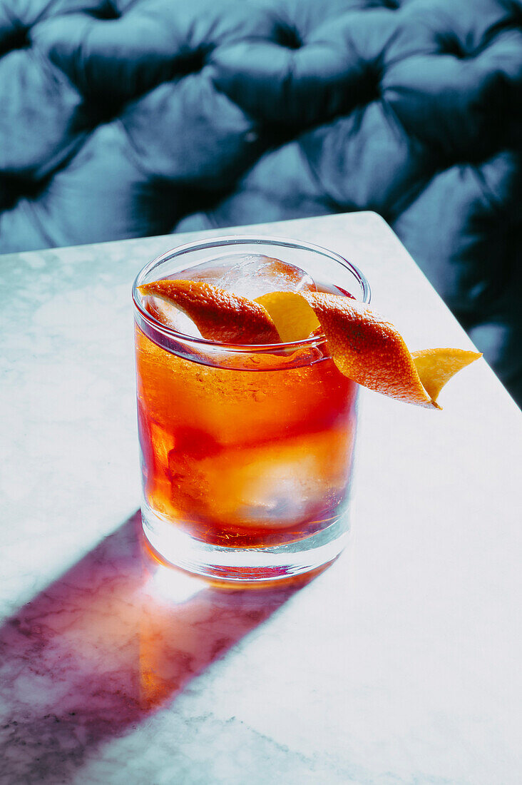 Glas mit altmodischem Cocktail und Eiswürfeln, verziert mit Orangenschalen, auf Marmoroberfläche