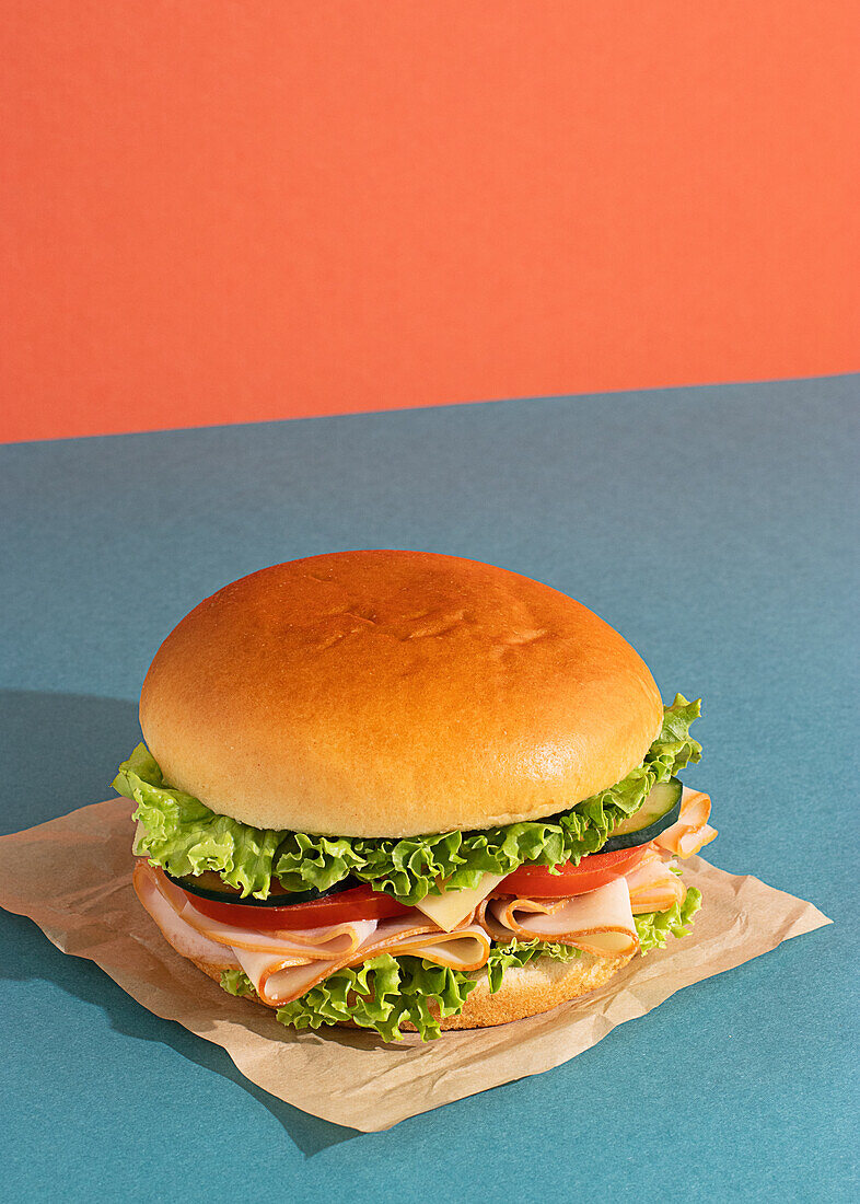 Delicious sandwich with ham, tomatoes, cucumber and cheese slices and fresh lettuce on blue and orange background