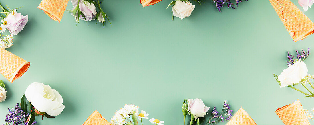 Flat lay of waffle cones and flowers on pastel green background, top view, flat lay. Spring or summer mood concept, banner, copy space