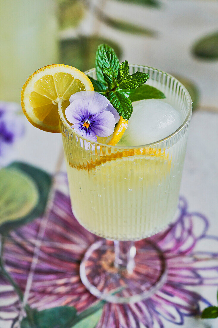 Zitronen-Minze-Limonade Mocktail auf floralem Hintergrund mit Zitrone, Minze und lila Blumendekor