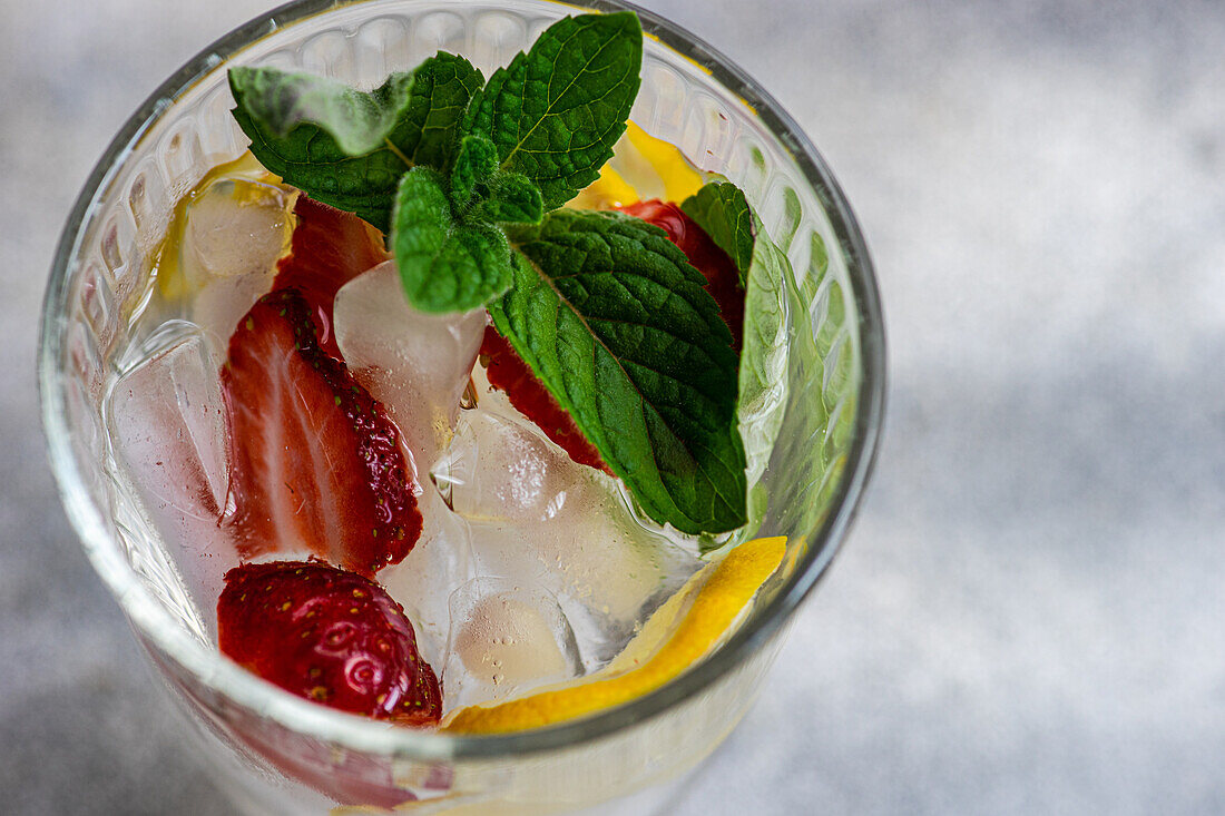 Draufsicht auf ein Sommercocktailglas mit Eis, Minze, Zitrone und Erdbeere im Glas vor unscharfem Hintergrund