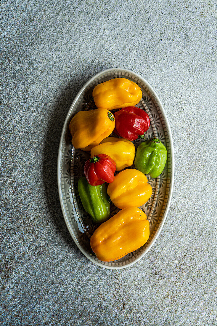 Top view of different colored peppers placed on a ceramic platter on a concrete background