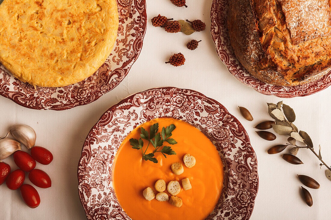 A cozy autumnal spread showcasing a tasty spanish omelette and a creamy salmorejo soup wit croutons and bread on decorative plates.