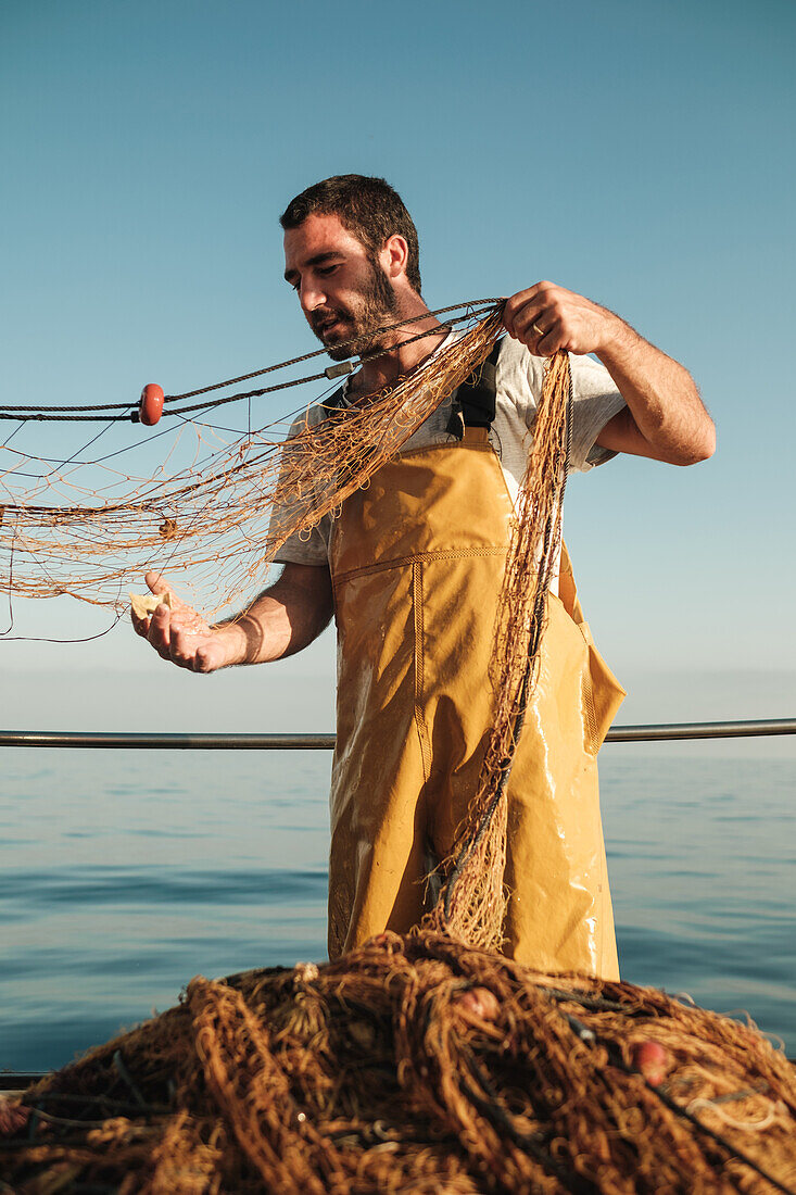 Focused bearded male fisher in uniform seiner hunting fish with net while working on schooner in Soller near Balearic Island of Mallorca