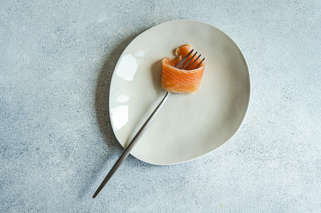 Top view of healthy salmon rolled on fork served on white plate against gray surface