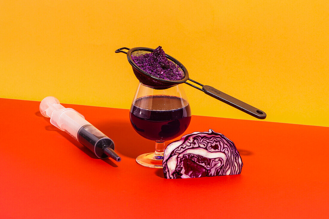 Composition of glass with strainer and syringe filled with homemade juice of red cabbage against bright background