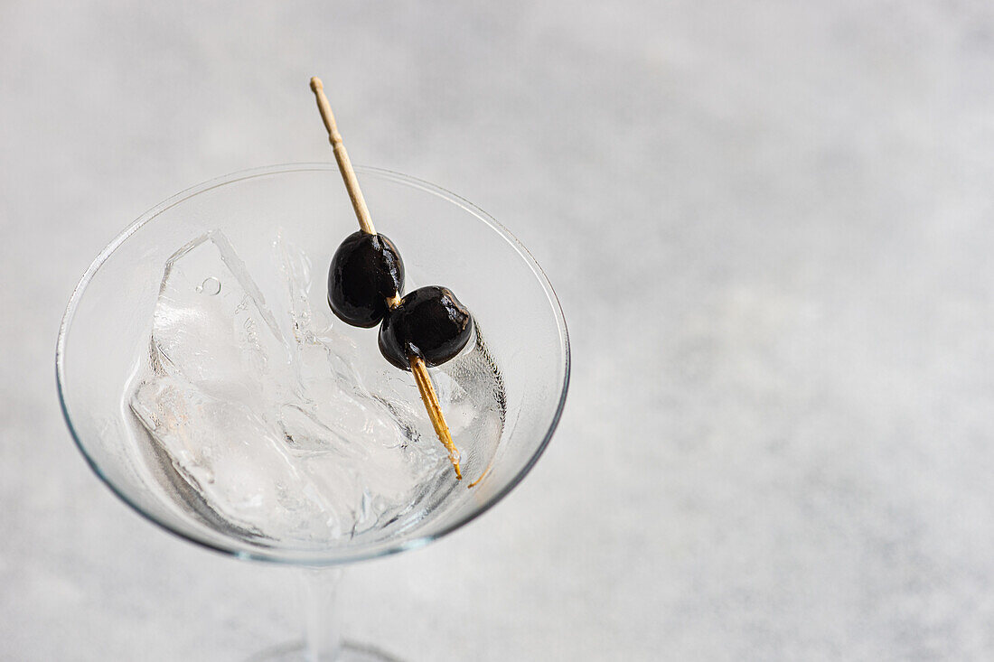 From above glass filled with alcohol martini vodka cocktail with black olives in martini glass on concrete table