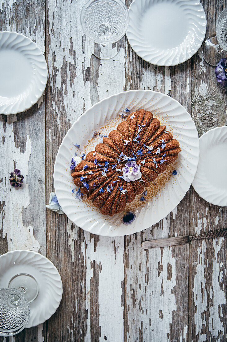 Von oben köstlicher süßer Schokoladenkuchen mit frischen Blumen auf einem weißen Keramikteller auf einem Holztisch mit Glaswaren