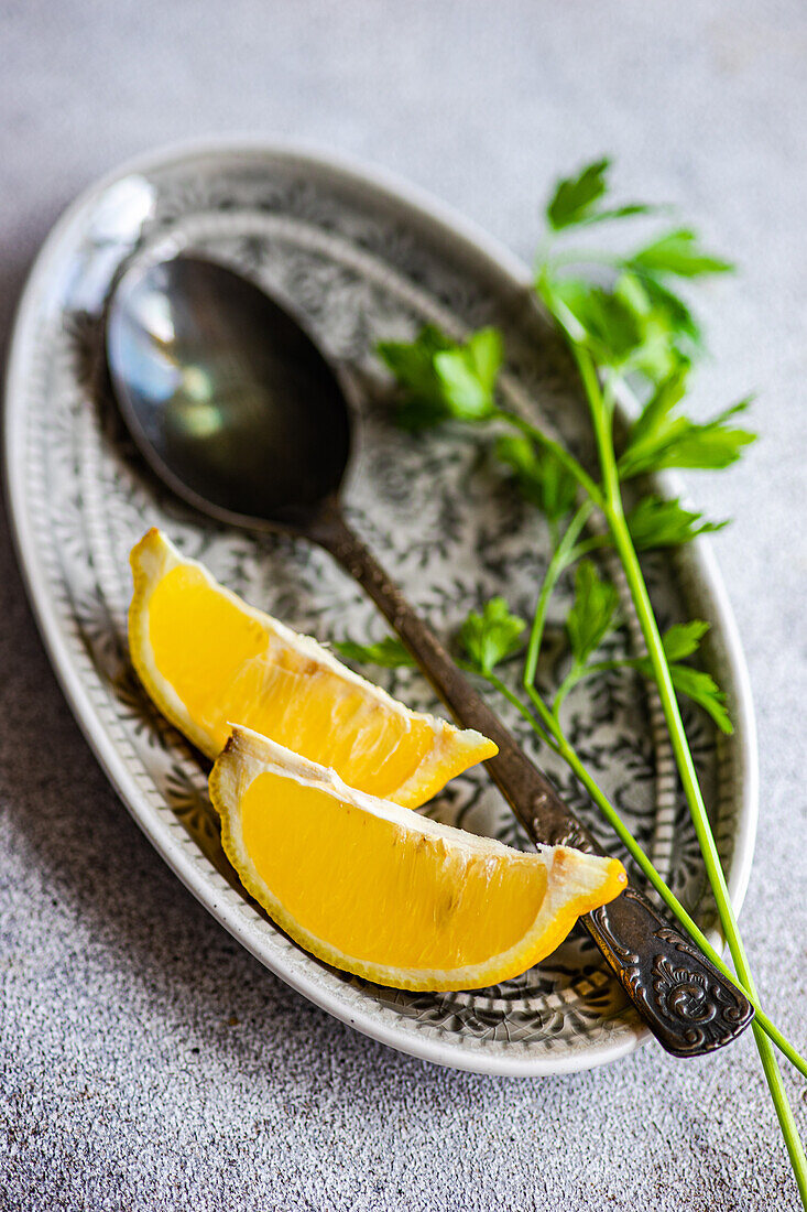 High angle of spoon with virgin olive oil, lemon slices and green parsley herb on plate against blurred background
