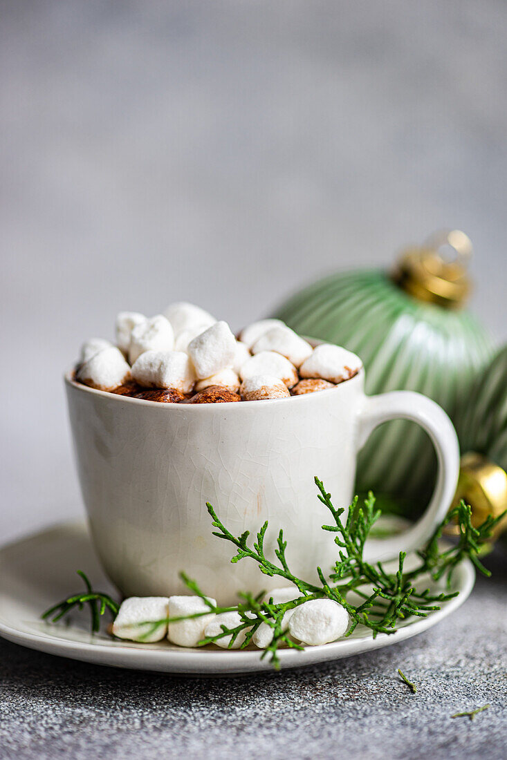 Focused of delicious cocoa with marshmallow on plate with fir twigs placed near Christmas balls