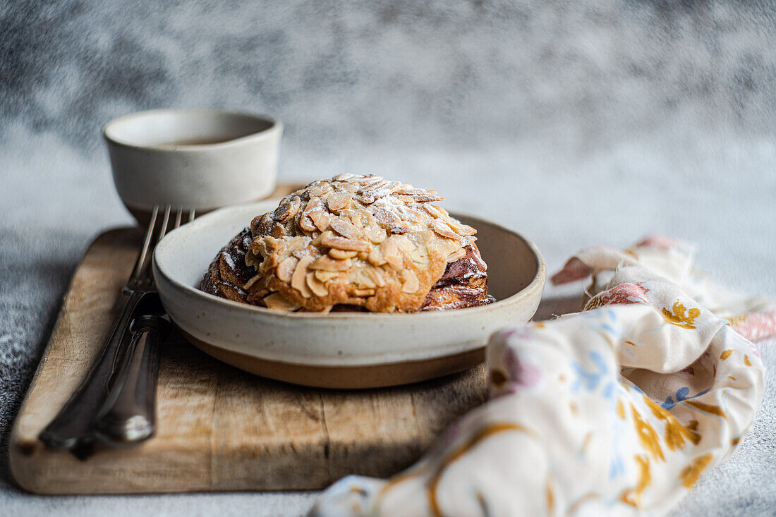 Closeup of sweet almond pastry on wooden chopstick between fork and knife and napkin with cup of green tea against blurred background