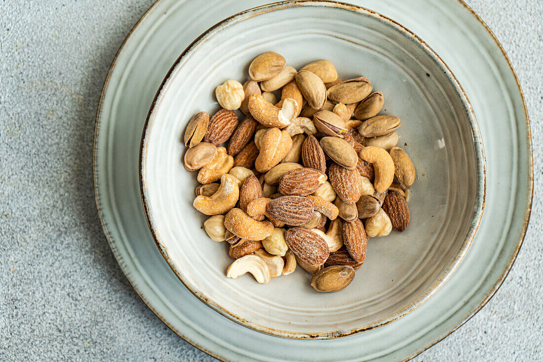 A mix of almonds, cashews, and other nuts presented in a rustic ceramic bowl on a textured gray surface