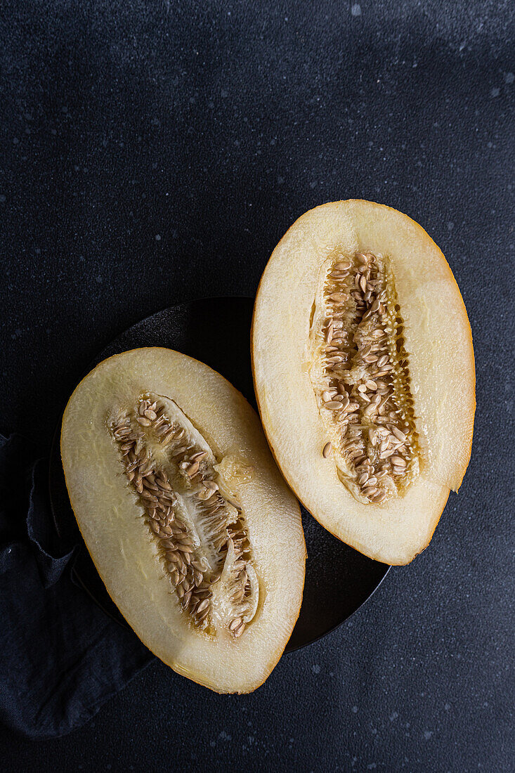 Draufsicht auf Scheiben von süßer, gerissener Melone, serviert in einem Keramikteller auf einem schwarzen Betontisch