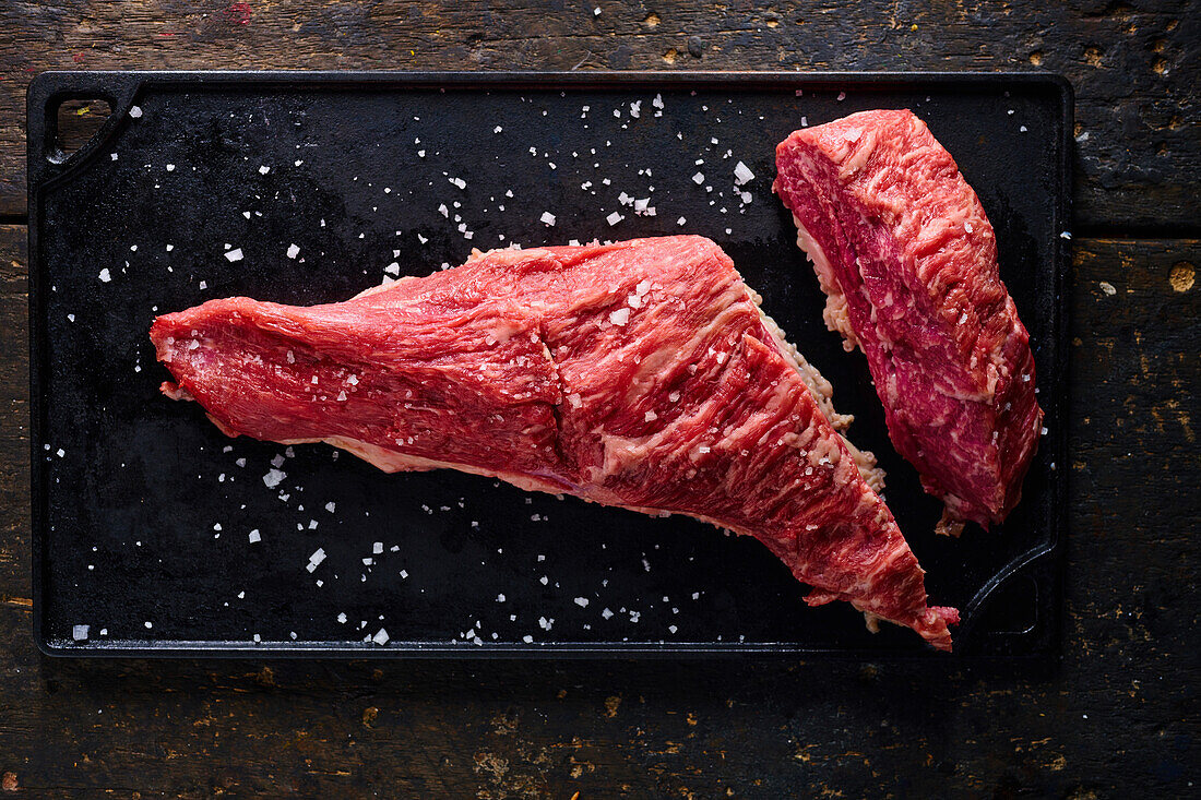 Top view of raw meat pieces placed on black tray sprinkled with salt for cooking traditional Ecuadorian dish