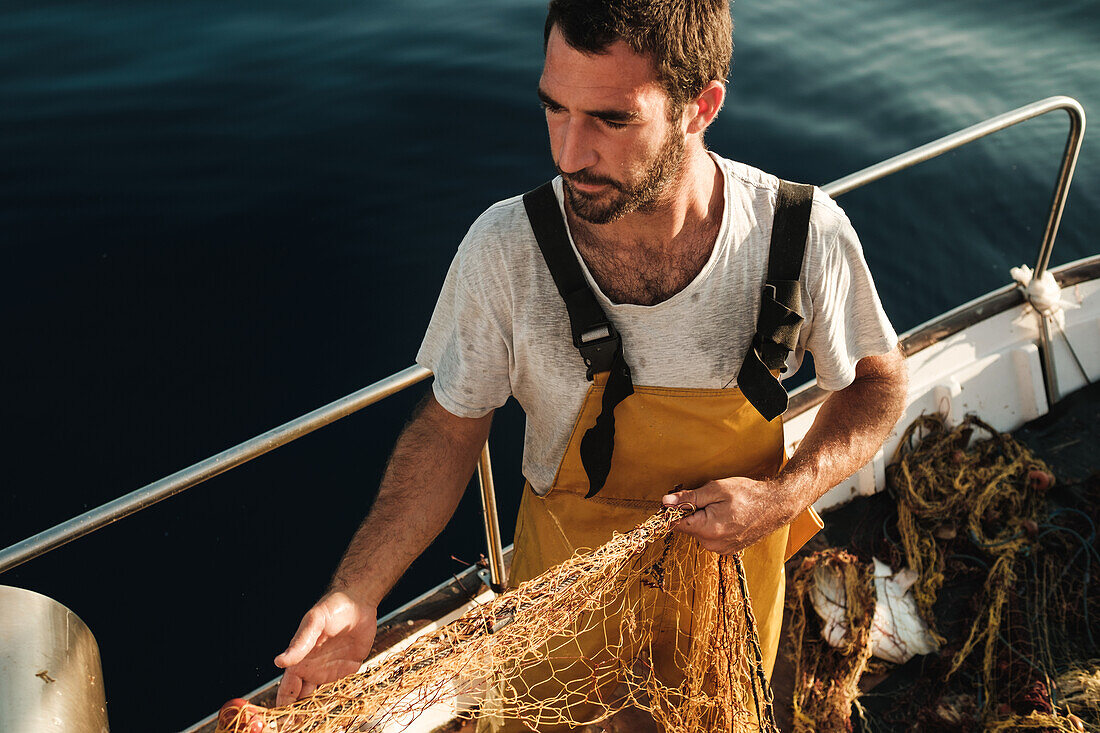 From above focused bearded male fisher in uniform seiner hunting fish with net while working on schooner in Soller near Balearic Island of Mallorca