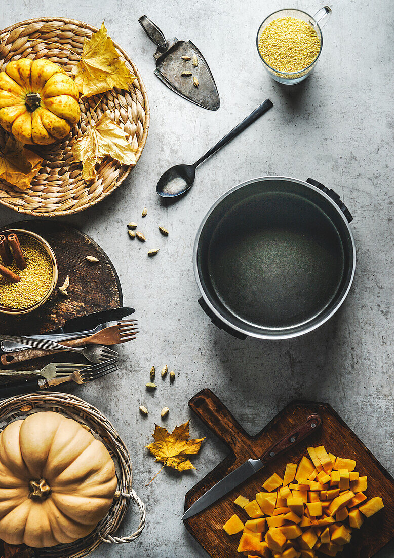 Leckere Kochvorbereitung mit verschiedenen Kürbissen, Kochtopf, Küchenutensilien und Gewürzen auf grauem Betontisch. Saisonales Herbstgemüse. Ansicht von oben