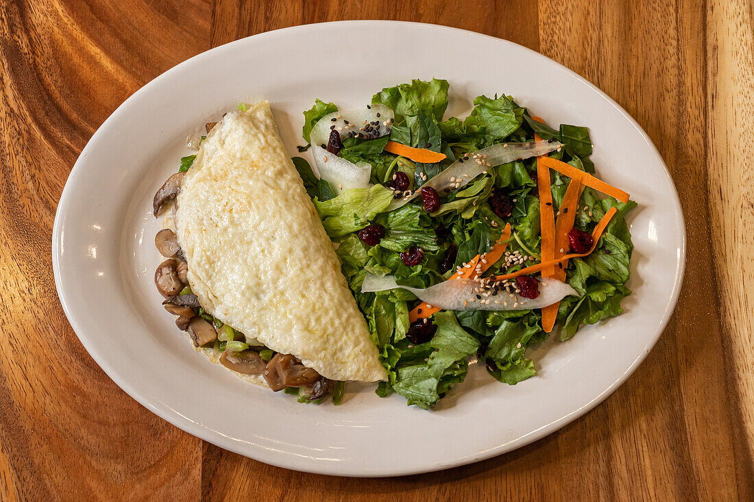 Top view of delicious omelette prepared with egg whites with finely cut mushrooms and vegetable herbs salad served on white plate on wooden table in light