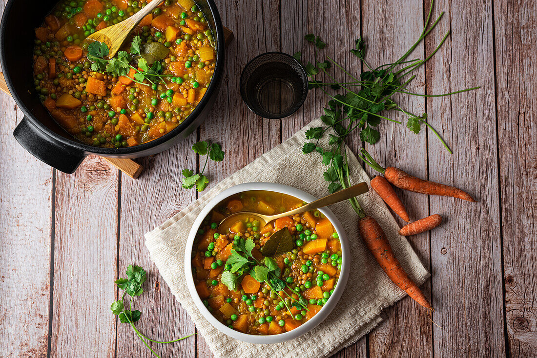 Top view of appetizing fresh cooked soup with carrot and green peas served in white ceramic bowl placed on wooden table and decorated with parsley branch