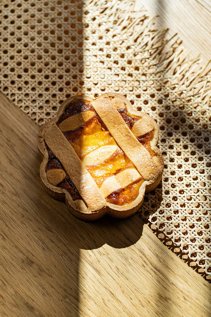 A sunlit Italian pastiera napoletana casts playful shadows on a wooden surface, surrounded by Easter elements.