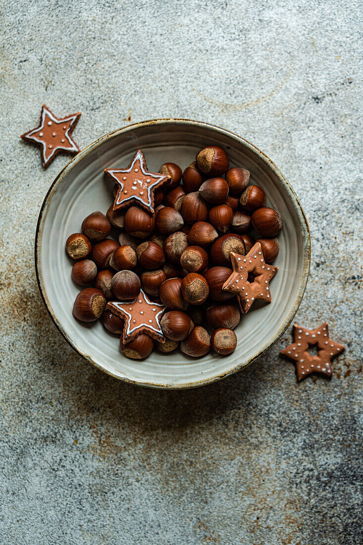 From above of plate of heap of chestnuts with tasty Christmas cookies placed on table in concrete grey background