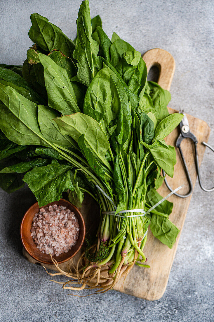 Top view of bunch of fresh spinach leaves on rustic wooden board accompanied by aromatic spices in bowl symbolizing healthy salad preparation