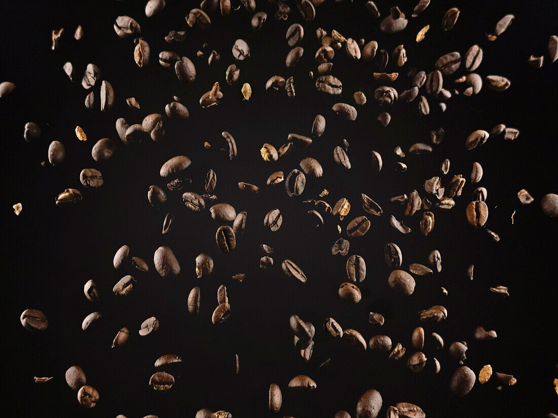 Fragrant roasted coffee beans falling against dark backdrop as concept of ingredient for tasty hot drink