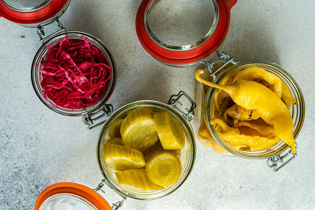 Overhead view of glass jars filled with colorful fermented vegetables, including cabbage with beetroot, spicy peppers, and pickled cucumbers.