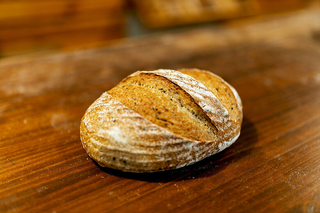 Closeup of freshly baked tasty loaf of bread with crispy crust placed on wooden table in kitchen at bakehouse