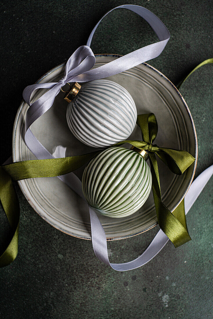 Top view of balls decorated with colorful satin ribbon as symbol of Christmas time placed ceramic bowl on gray surface