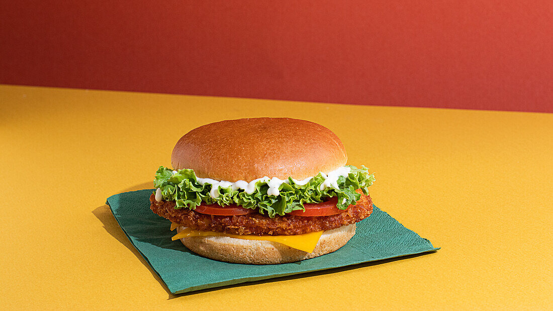 Delicious fish burger with tomatoes, cheese slices and fresh lettuce on yellow and red background