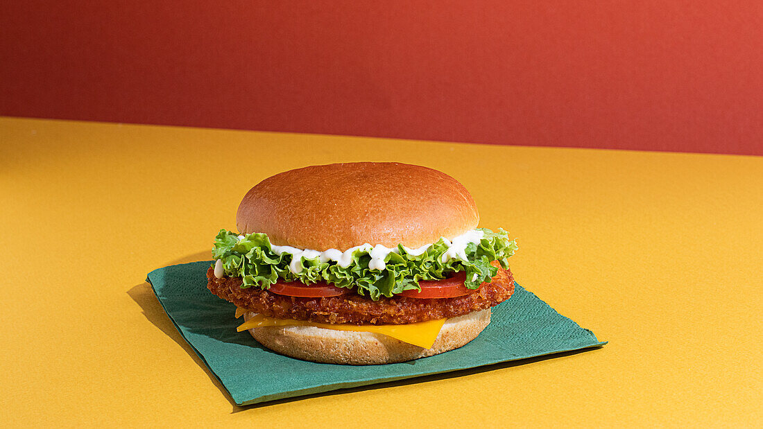 Leckerer Fisch-Burger mit Tomaten, Käsescheiben und frischem Salat auf gelbem und rotem Hintergrund