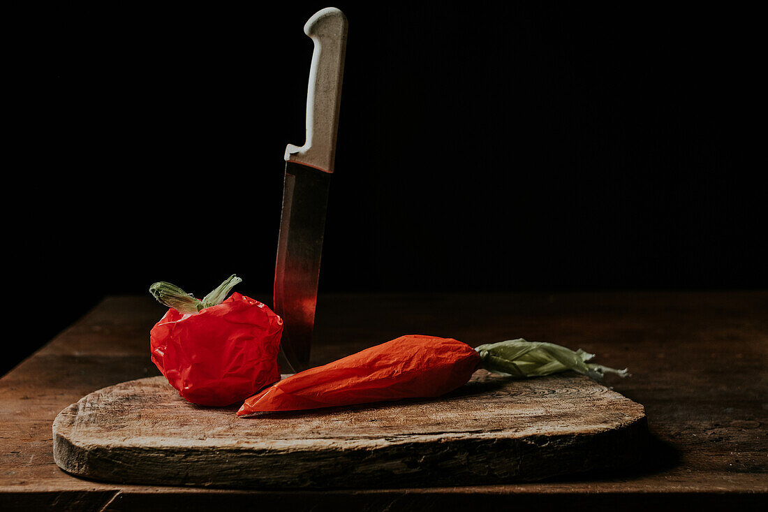 Plastic bags crafted to resemble a tomato and carrot alongside a kitchen knife on a rustic wooden chopping board