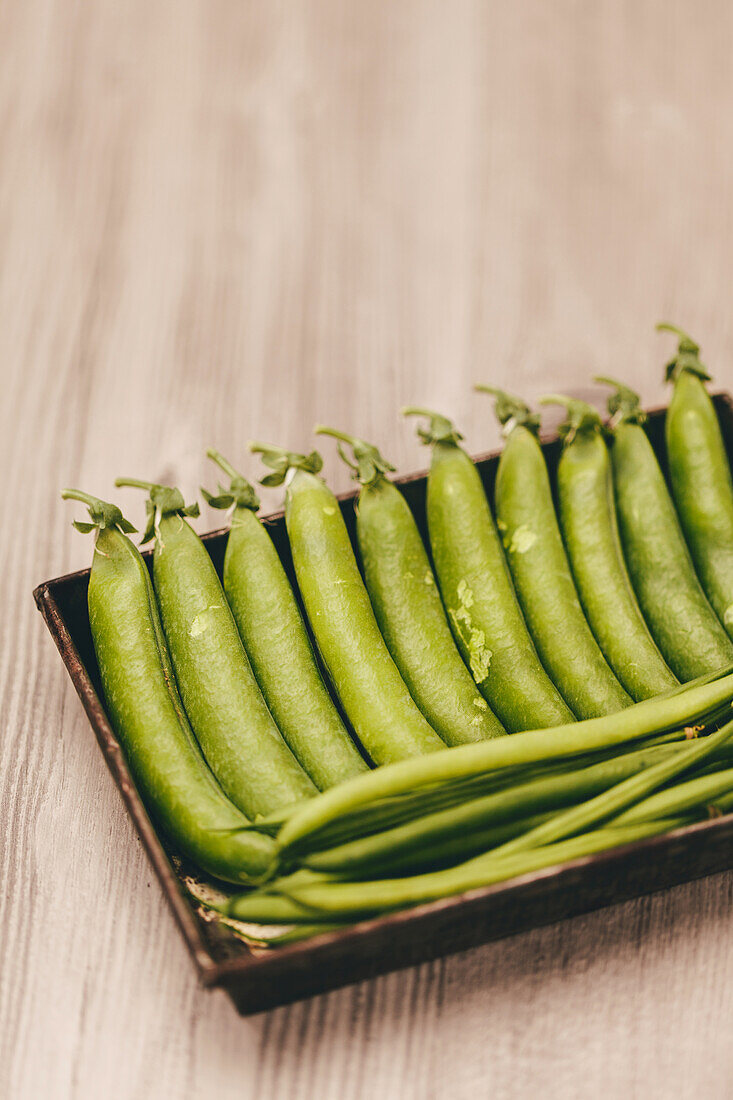 A close-up image showcasing vibrant green peas in a pod neatly arranged in a rustic wooden box, set against a soft wooden background.