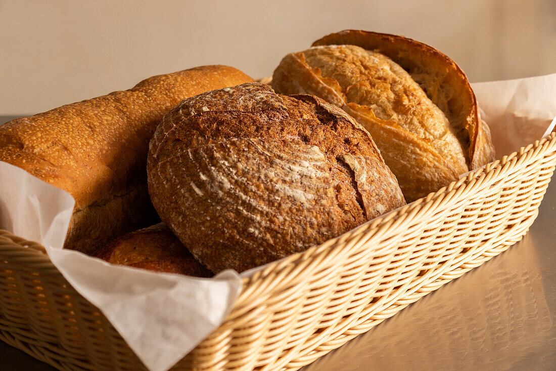 Various tasty freshly baked pastry breads being served with baking pan into wicker basket with fabric on dining table indoors