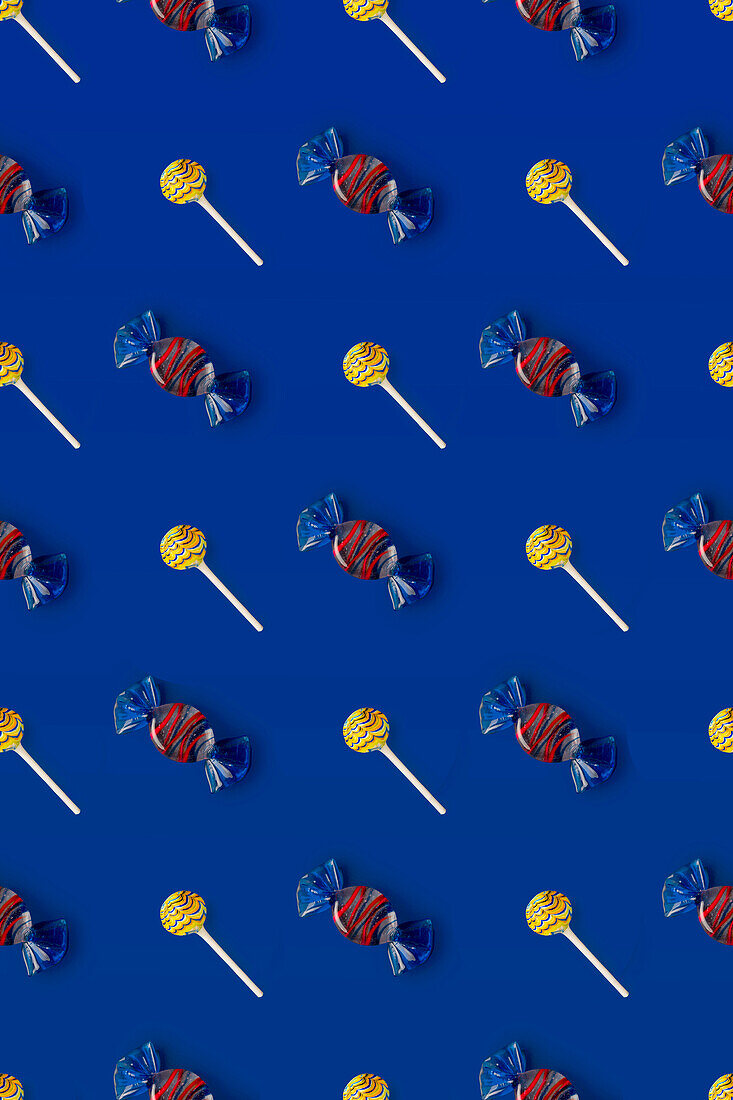 Top view of pattern of whole sweet crystal candies and lollipops arranged on blue background