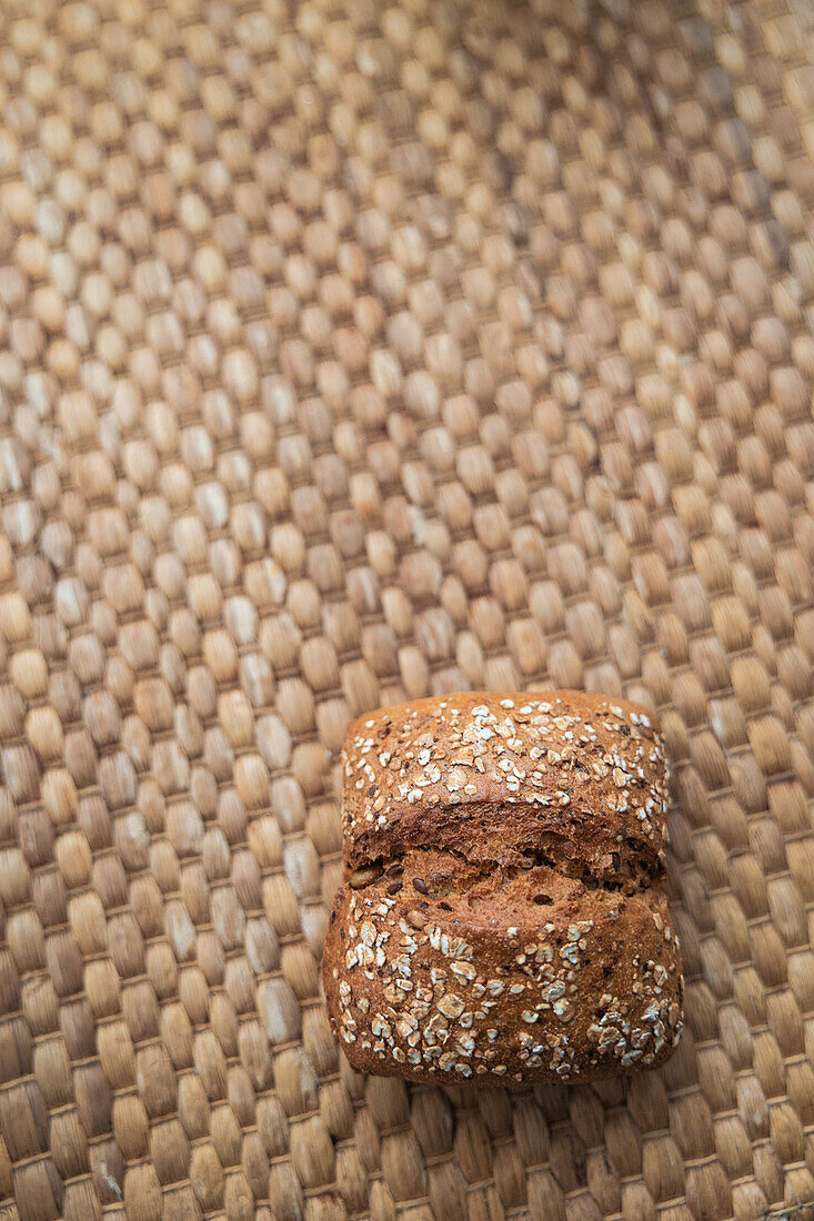 A freshly baked loaf of brown bread with seeds, resting on a textured, woven mat, exemplifying rustic simplicity