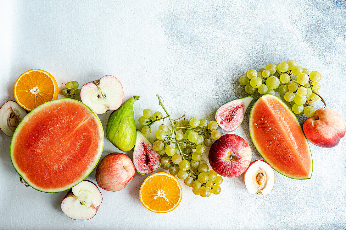 Top view of seasonal fruit frame consisting of watermelon, grapes, orange, pear and apple placed on white surface