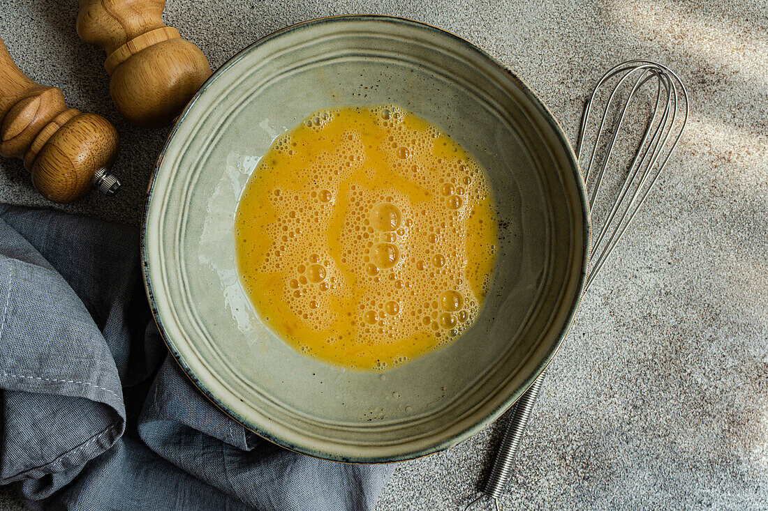 Top view of raw whisked egg in bowl while cooking at concrete table with in kitchen