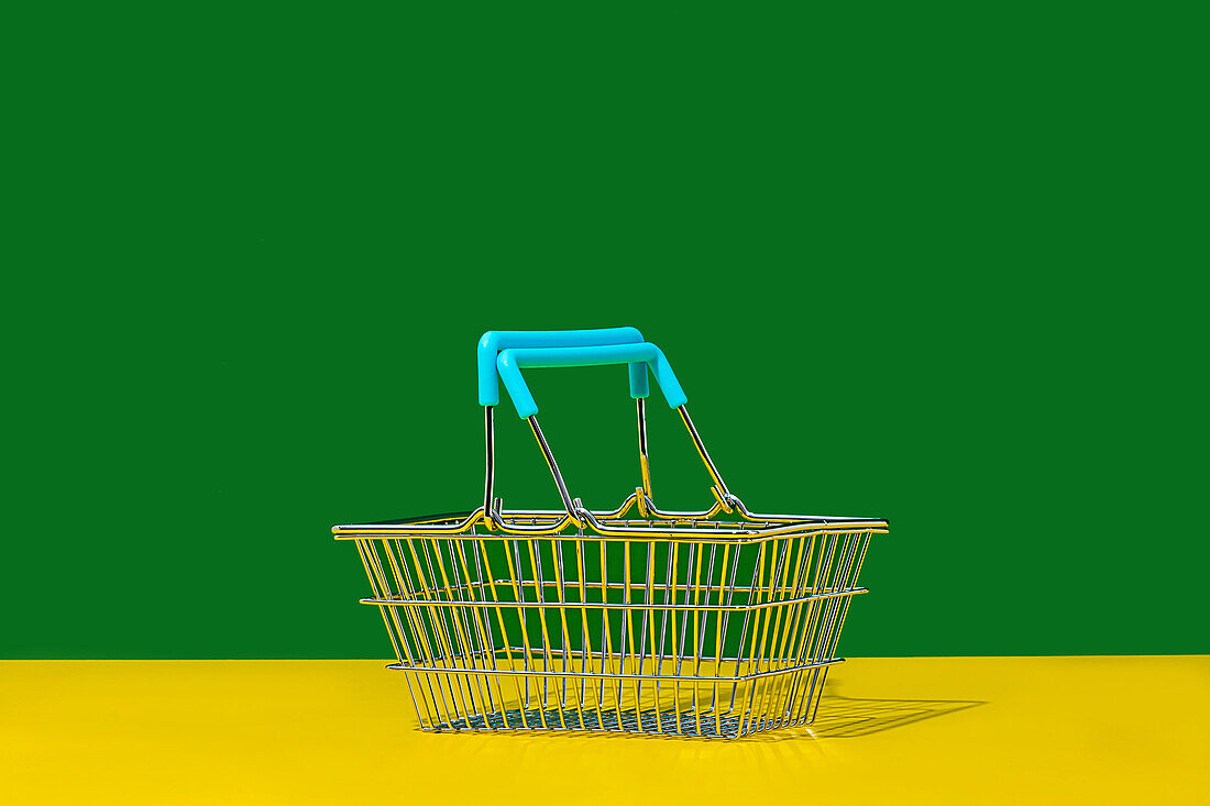 Empty metal basket with blue handles placed on yellow table against green wall