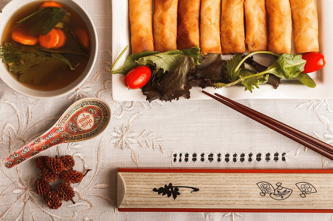 Asiatisches Essgeschirr mit vietnamesischen Brötchen auf einem Teller, einer Schale mit Suppe, Reis und Stäbchen